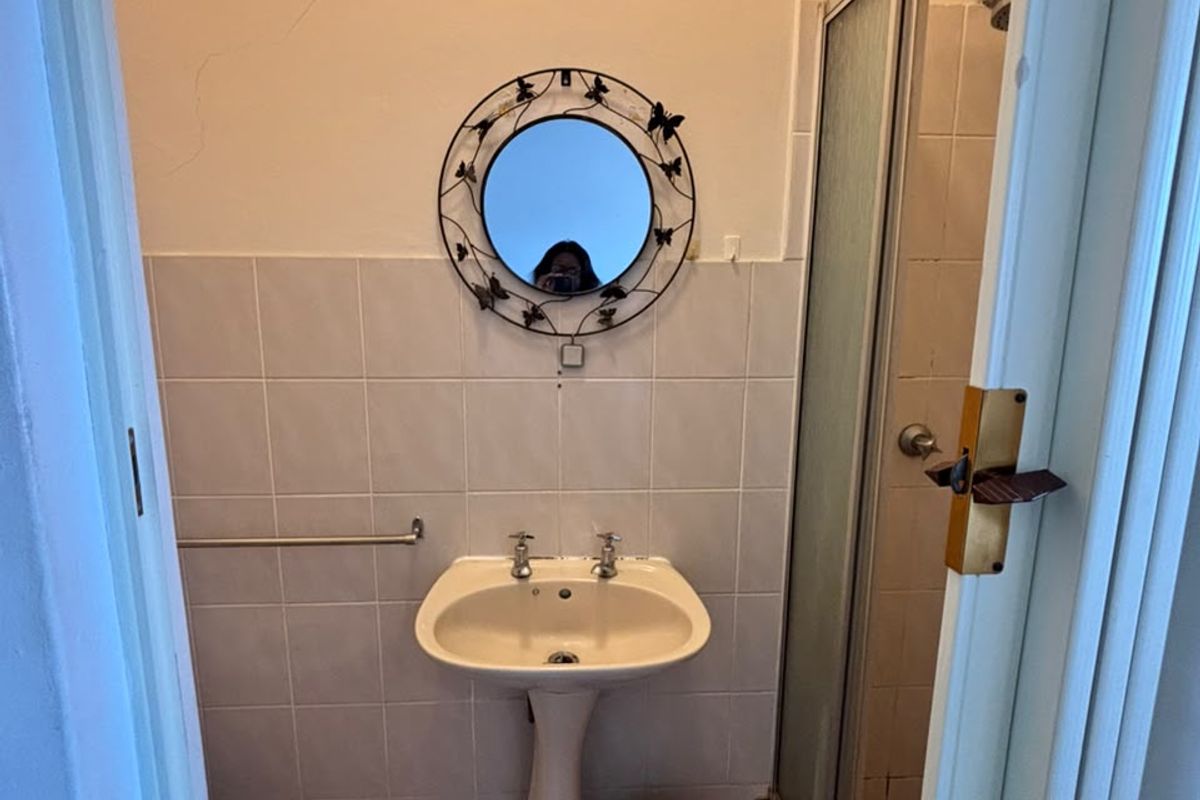 A compact bathroom featuring a pedestal basin, tiled splashback, and a shower enclosure with a glass door.