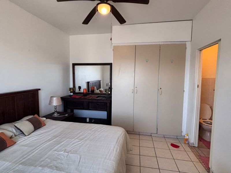 A bedroom featuring tiled flooring, a ceiling fan, and built-in cupboards, with direct access to an en-suite bathroom.