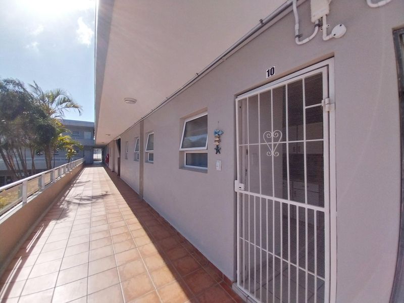 Exterior view of an apartment unit entrance featuring a tiled walkway, security gate, and building facade.