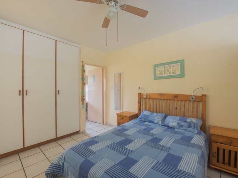 A functional bedroom featuring built-in cupboards, tiled flooring, and a ceiling fan, providing a comfortable and practical living space.
