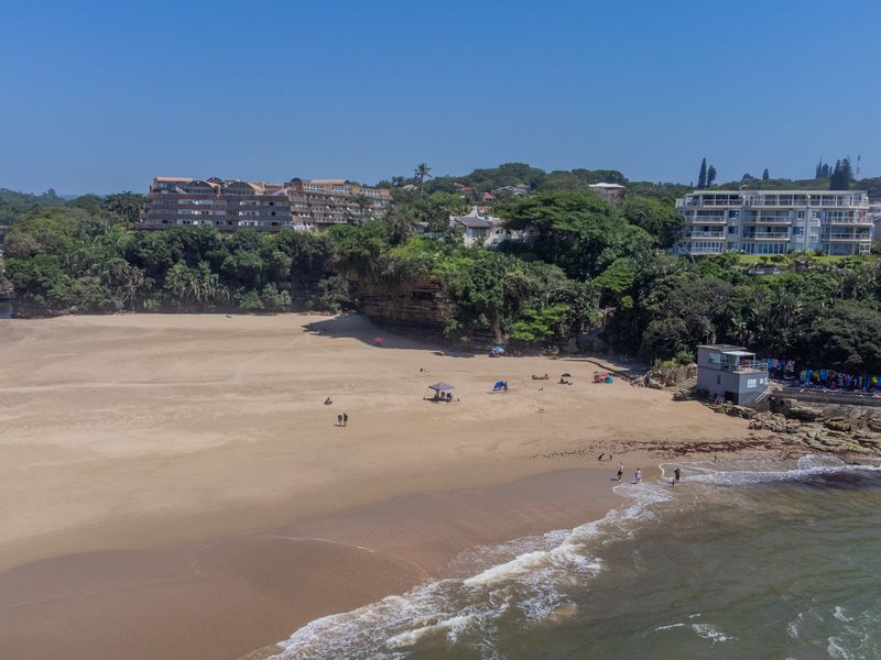 Aerial view of the coastal landscape featuring sandy beach, ocean shoreline, and surrounding residential apartment complexes.
