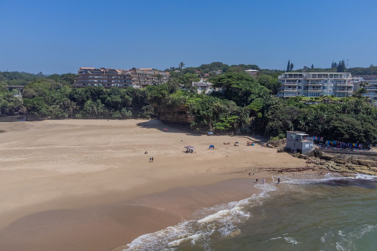 Aerial view of the coastal landscape featuring sandy beach, ocean shoreline, and surrounding residential apartment complexes.