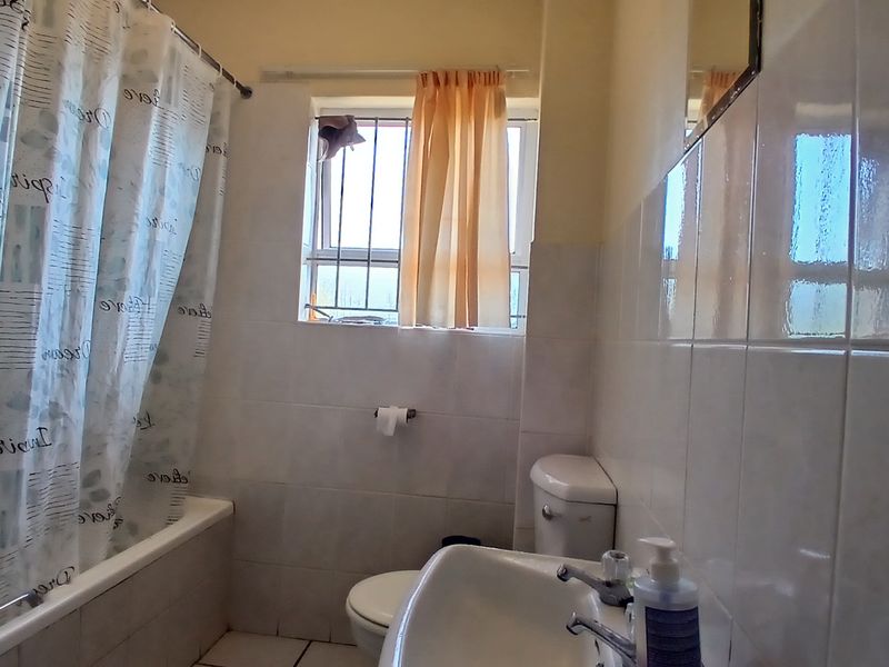 A functional bathroom featuring a bathtub, pedestal basin, and toilet with tiled walls and a window with security bars.