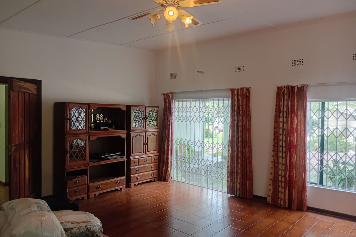 Spacious living room featuring tiled flooring, a ceiling fan, and large windows secured with metal security gates.