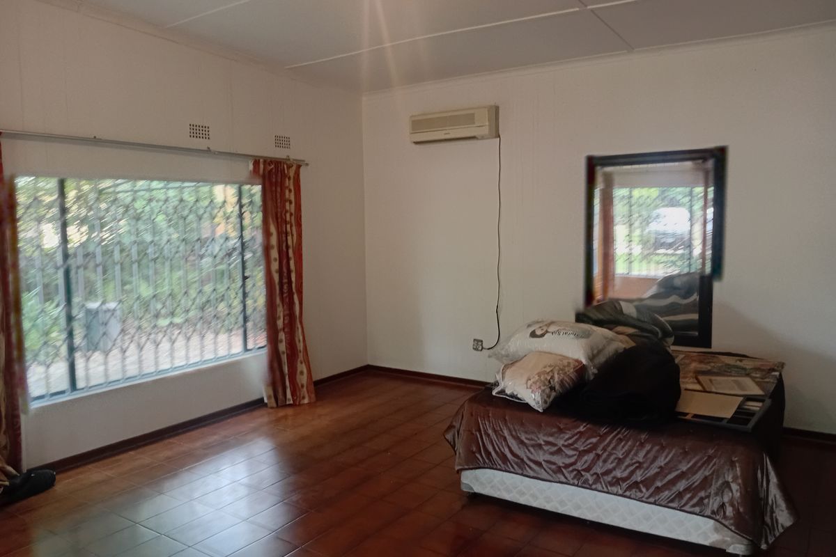 A bedroom featuring tiled flooring, a wall-mounted air conditioning unit, and large windows fitted with security bars.