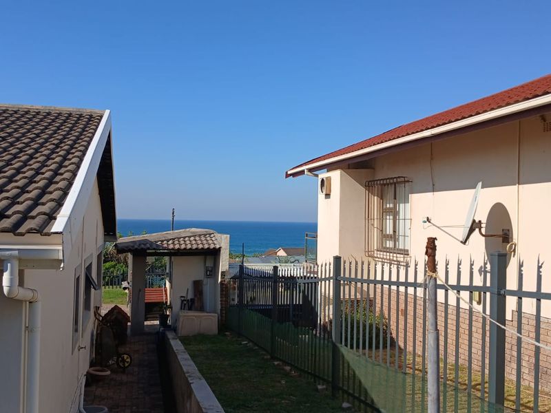 Rear exterior view of the cottage showing a side pathway, metal security fencing, and a clear view of the ocean in the distance.