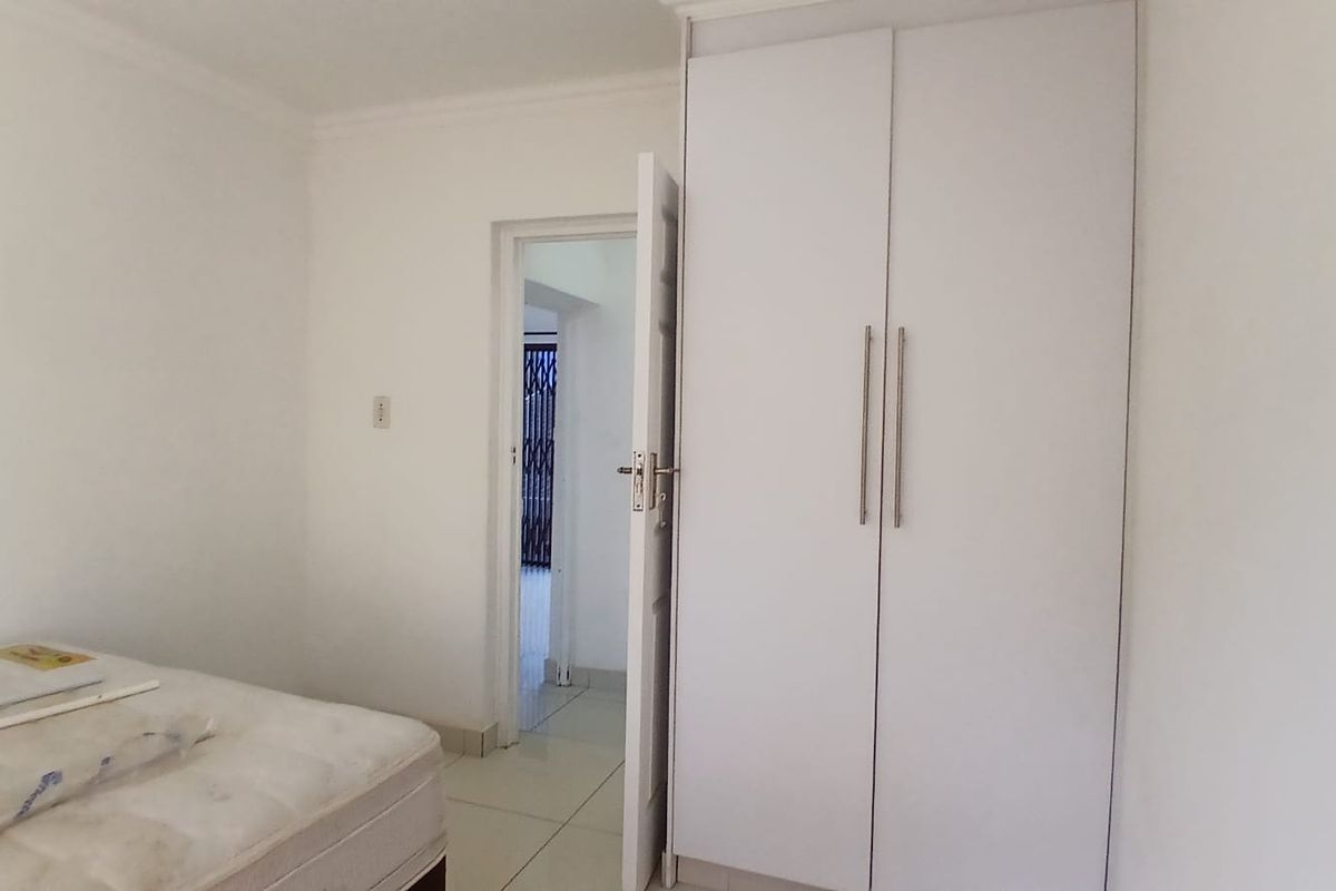 A simple bedroom featuring white built-in wardrobes and tiled flooring, offering a clean and neutral space ready for personalization.