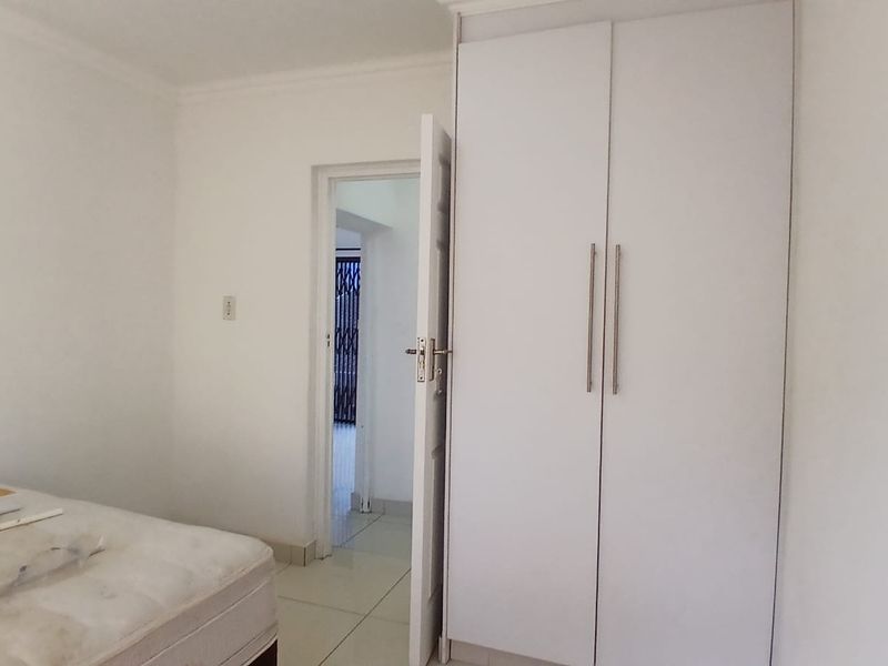 A simple bedroom featuring white built-in wardrobes and tiled flooring, offering a clean and neutral space ready for personalization.
