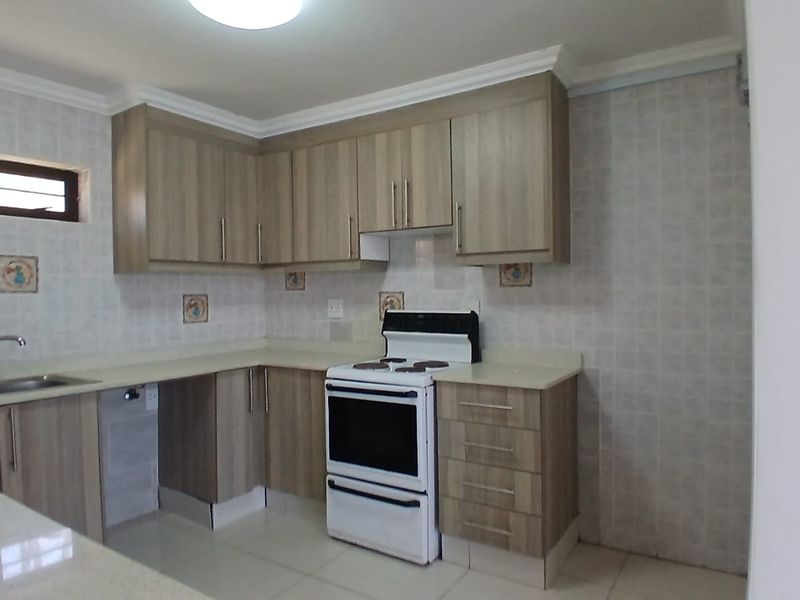 A functional kitchen featuring light wood-tone cabinetry, stone countertops, tiled backsplash, and a freestanding electric stove in a clean, well-maintained space.