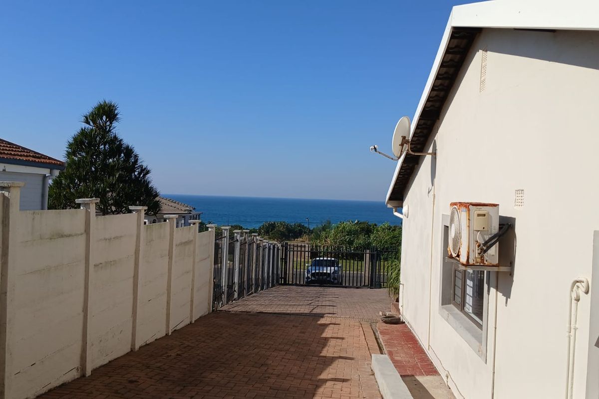 Rear exterior view of the cottage featuring a paved driveway, precast boundary wall, and a clear view of the ocean in the distance.