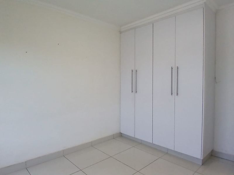 A clean, empty bedroom featuring neutral tiled flooring and modern white built-in cupboards with sleek handles.