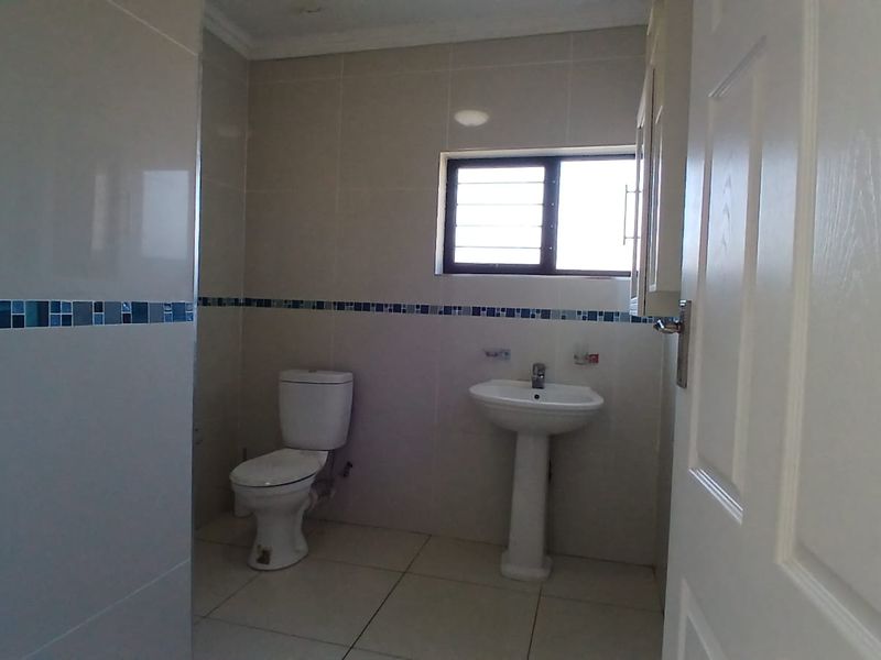 A clean, functional bathroom featuring a pedestal sink, toilet, and neutral wall tiles with a decorative mosaic border.