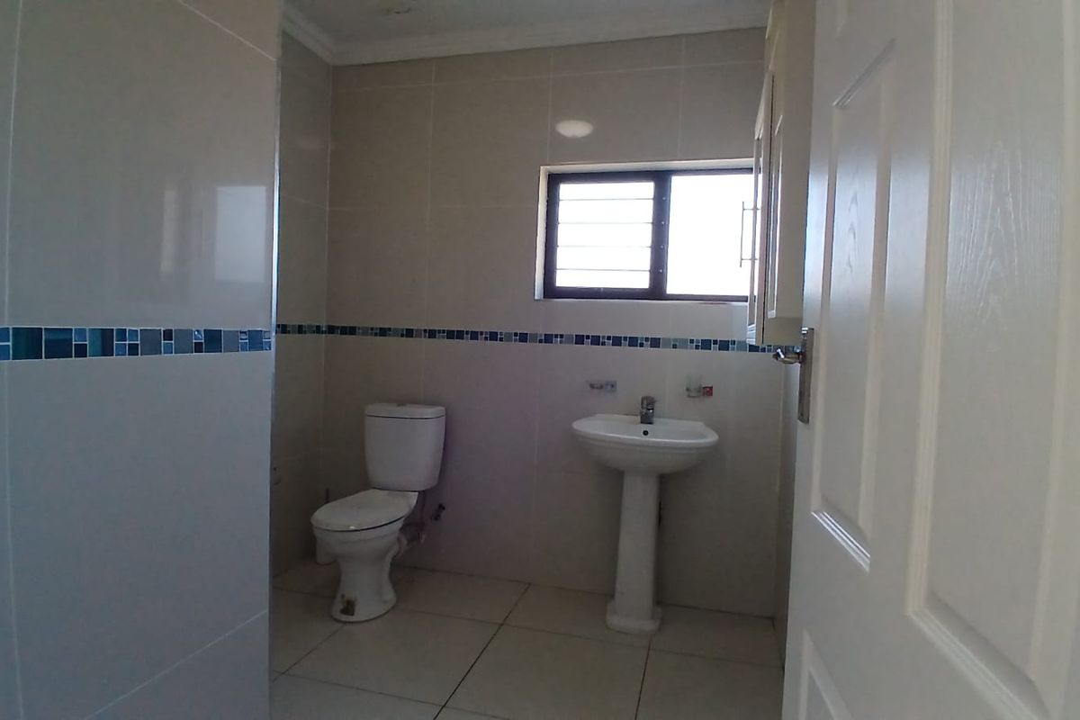 A clean, functional bathroom featuring a pedestal sink, toilet, and neutral wall tiles with a decorative mosaic border.