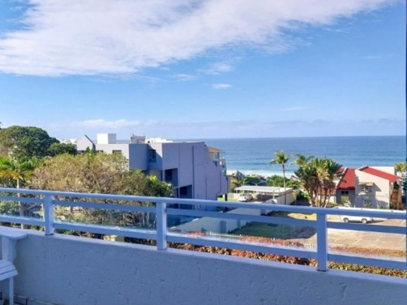 A scenic view of the ocean and surrounding neighborhood captured from an elevated balcony with white metal railings.