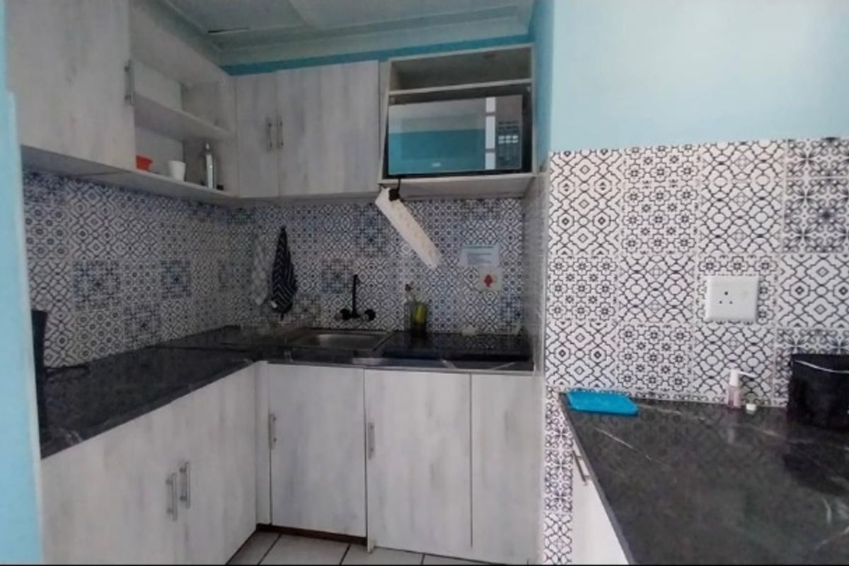 Compact kitchen featuring light wood-look cabinetry, dark countertops, and a decorative patterned tile backsplash with integrated microwave and sink.