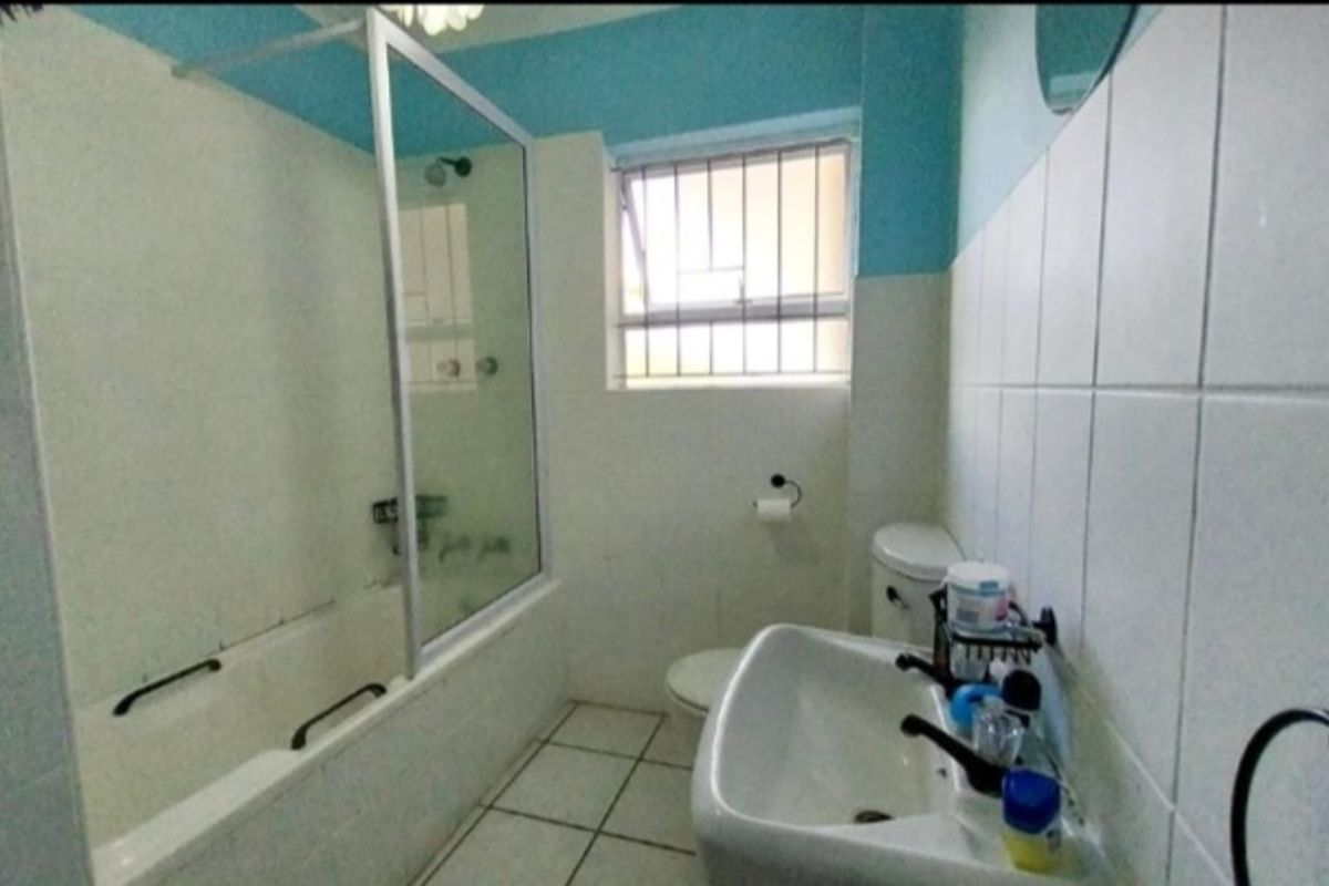 A functional bathroom featuring a bathtub with a glass screen, pedestal basin, and toilet, finished with tiled walls and flooring.