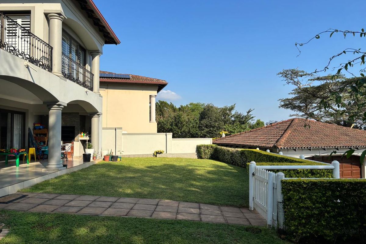 A well-maintained rear garden featuring a manicured lawn, paved walkway, and a covered patio area with structural columns.