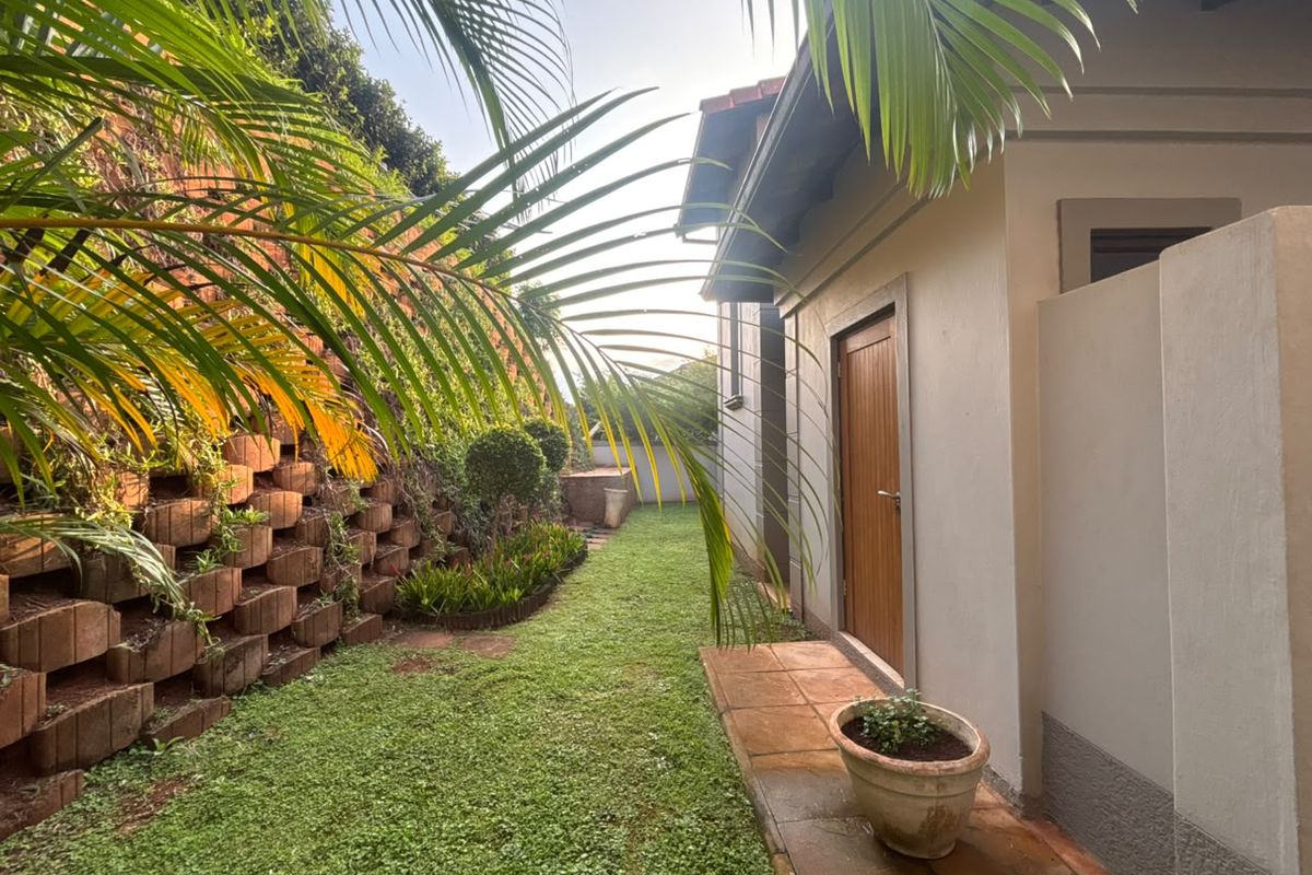 A well-maintained rear garden area featuring a tiered retaining wall, a paved walkway, and access to the home via a timber door.