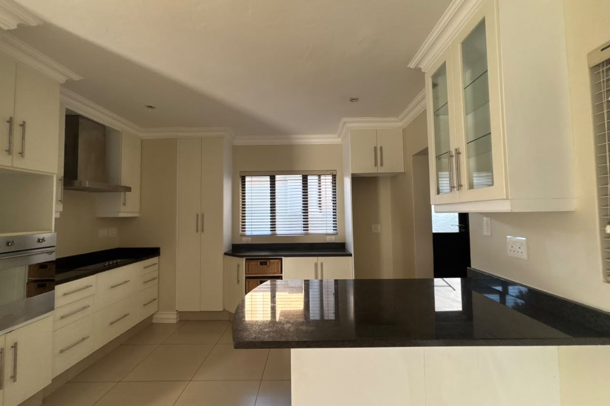 A clean, modern kitchen featuring white cabinetry, dark granite countertops, built-in stainless steel appliances, and neutral floor tiles.