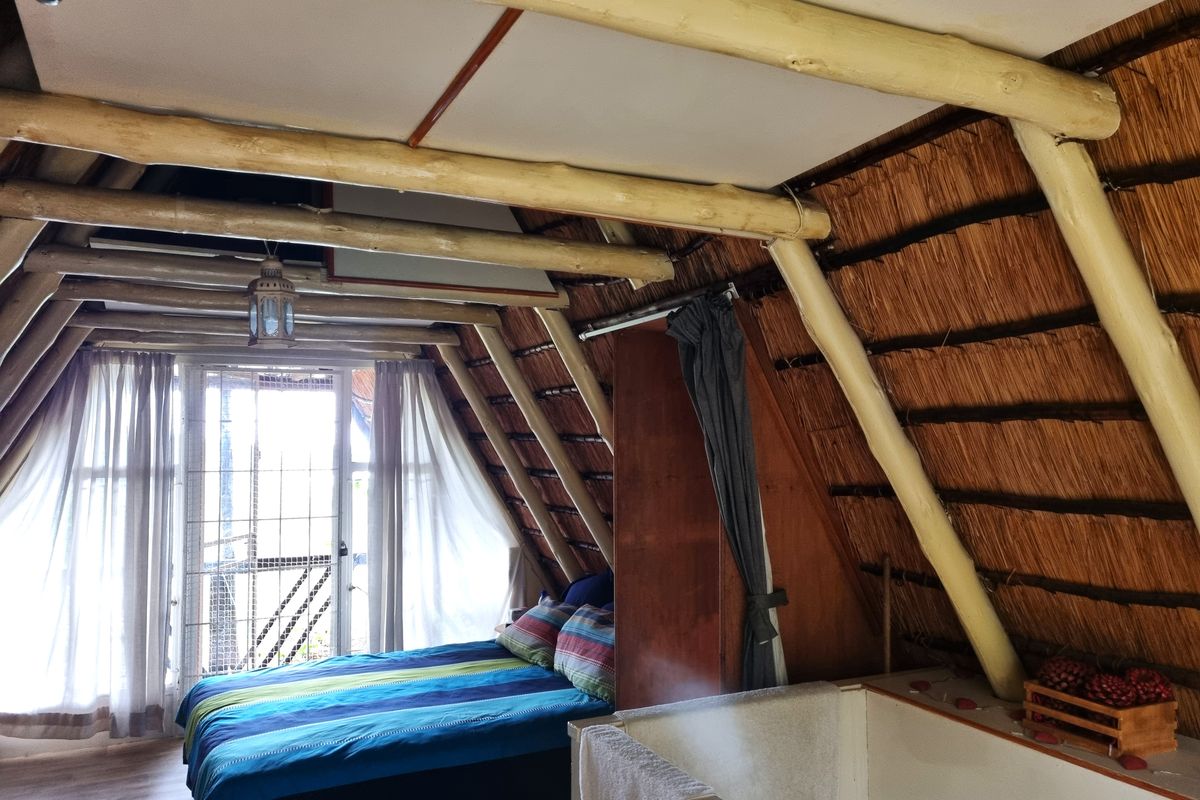A rustic bedroom featuring a distinctive A-frame design with exposed timber rafters, a thatched roof interior, and access to an outdoor area via sliding doors.