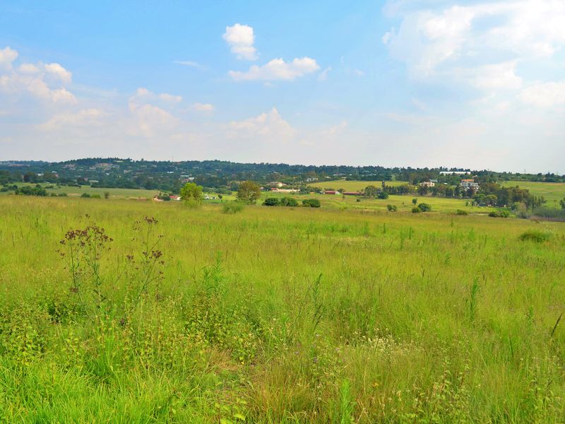 A wide-angle view of an expansive, undeveloped residential plot featuring natural grassland and distant rural landscape scenery.
