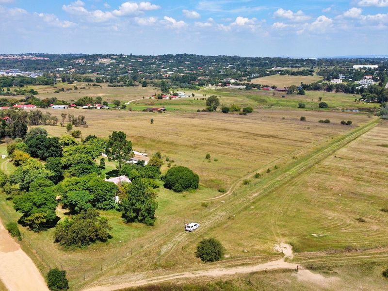 An aerial view of a large, undeveloped residential land parcel featuring open fields, mature trees, and access via a dirt road.