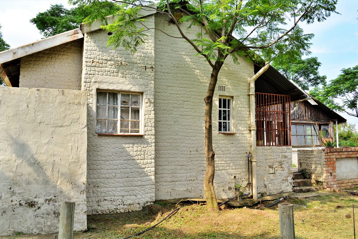 Rear view of a residential structure featuring textured masonry walls, metal window frames with security bars, and weathered exterior finishes.