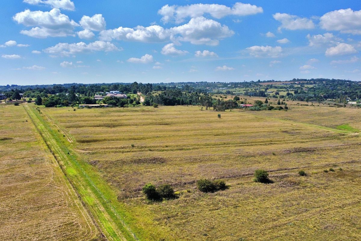 An aerial view of a large, open residential vacant land plot featuring natural grass coverage and perimeter fencing.