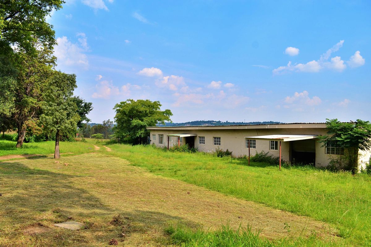 Rear view of a single-story residential structure on a large plot of land, featuring a covered patio area and surrounding grassy grounds.