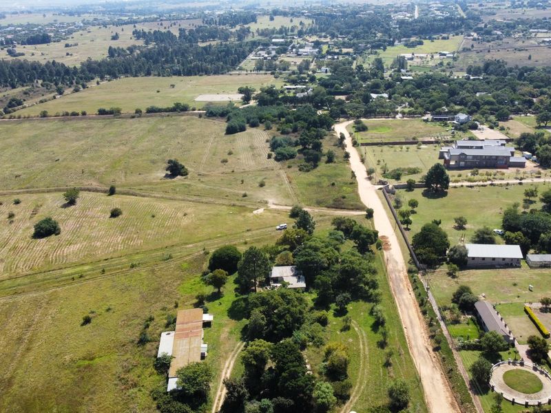 An aerial view of a large, undeveloped residential land parcel featuring natural vegetation, surrounding rural landscape, and access via a dirt road.