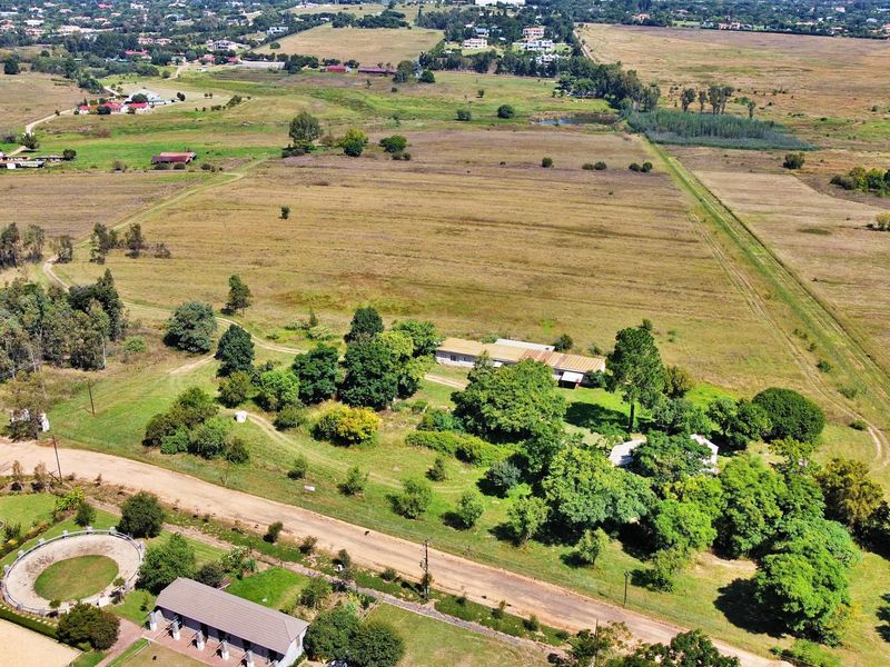 An aerial view of a large residential land parcel featuring mature trees, existing structures, and access roads within a rural landscape.