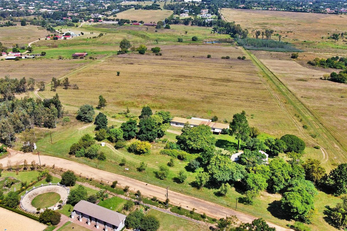 An aerial view of a large residential land parcel featuring mature trees, existing structures, and access roads within a rural landscape.