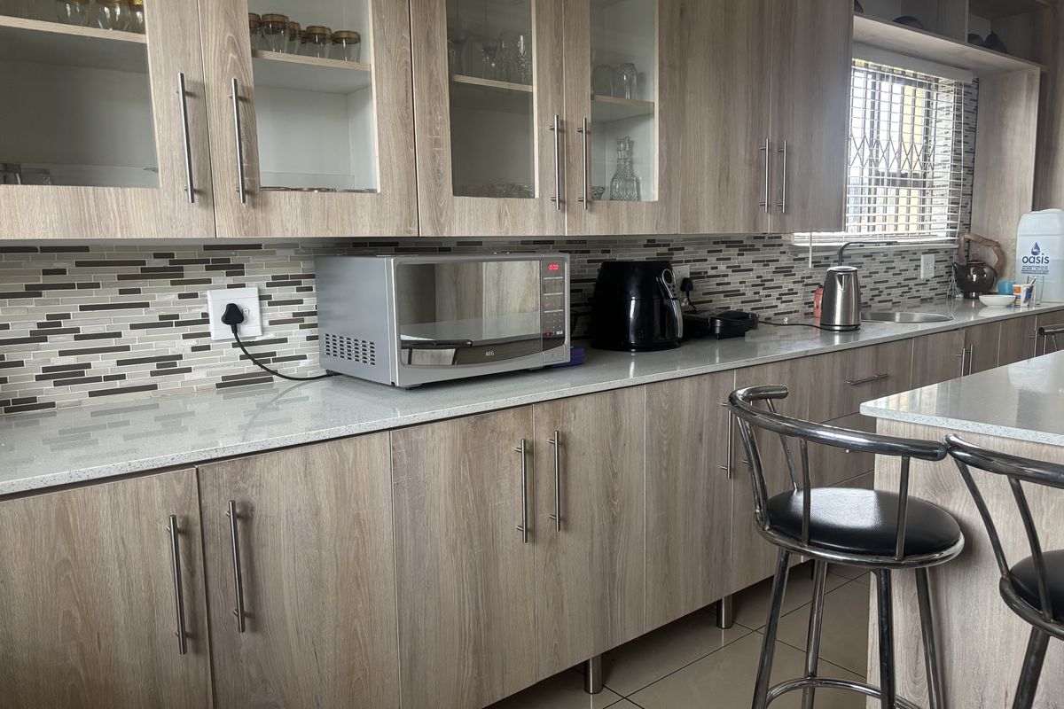 Modern kitchen featuring light wood-grain cabinetry, stone countertops, and a decorative mosaic tile backsplash with ample storage and workspace.