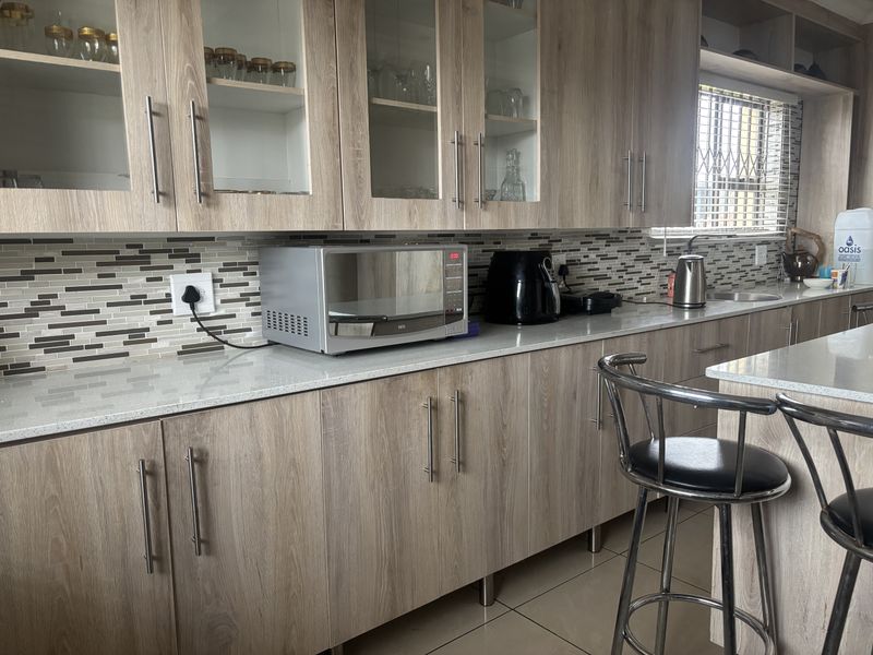 Modern kitchen featuring light wood-grain cabinetry, stone countertops, and a decorative mosaic tile backsplash with ample storage and workspace.