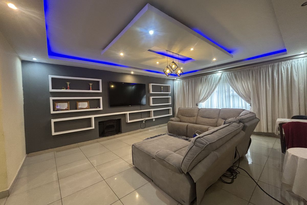 Modern living room featuring a recessed ceiling with ambient LED lighting, built-in wall shelving, a fireplace, and polished tiled flooring.
