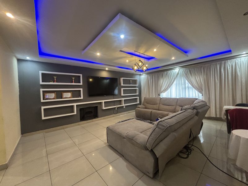 Modern living room featuring a recessed ceiling with ambient LED lighting, built-in wall shelving, a fireplace, and polished tiled flooring.