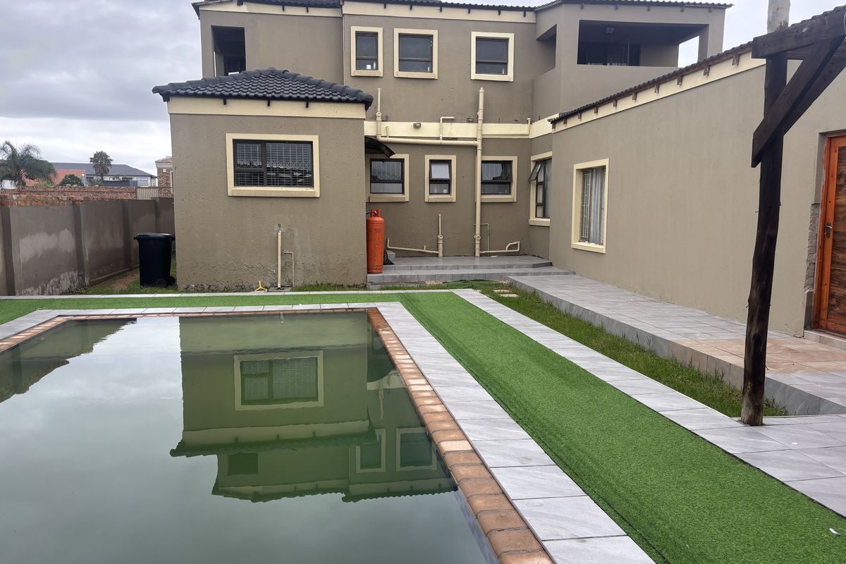 Rear exterior view of a two-story house featuring a swimming pool, tiled patio area, and artificial lawn with perimeter walling.