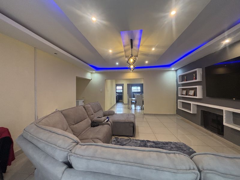 Spacious open-plan living area featuring a modern recessed ceiling with ambient LED lighting, tiled floors, and built-in wall shelving with an integrated fireplace.