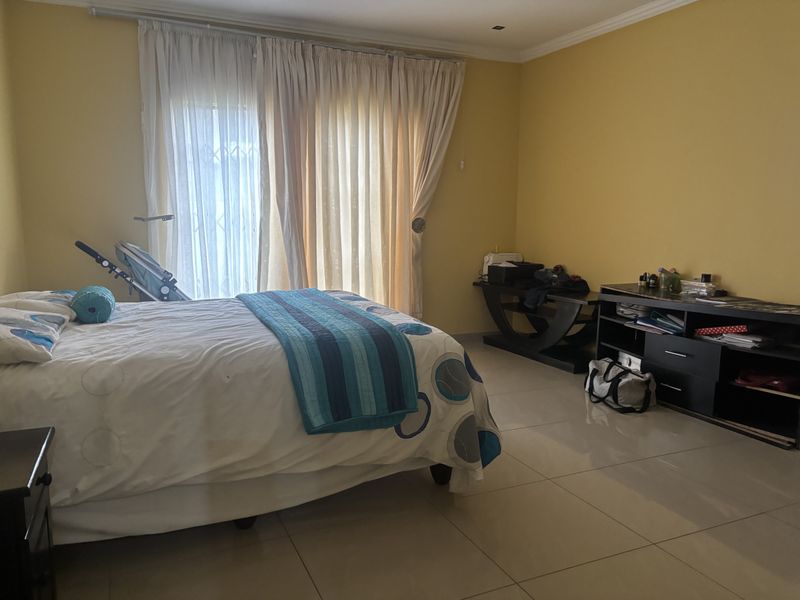 A spacious bedroom featuring large sliding glass doors with curtains, neutral tiled flooring, and recessed ceiling lighting.