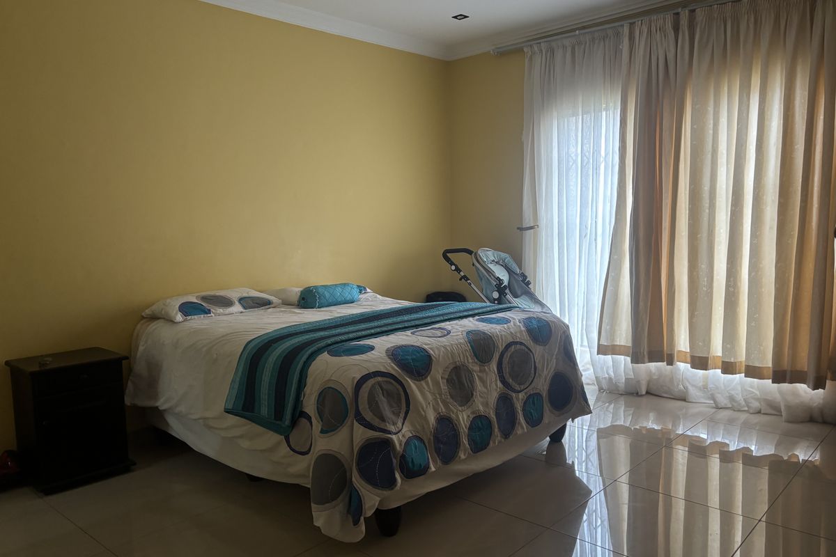 A spacious bedroom featuring tiled flooring, recessed lighting, and a sliding glass door with security gate providing access to the exterior.