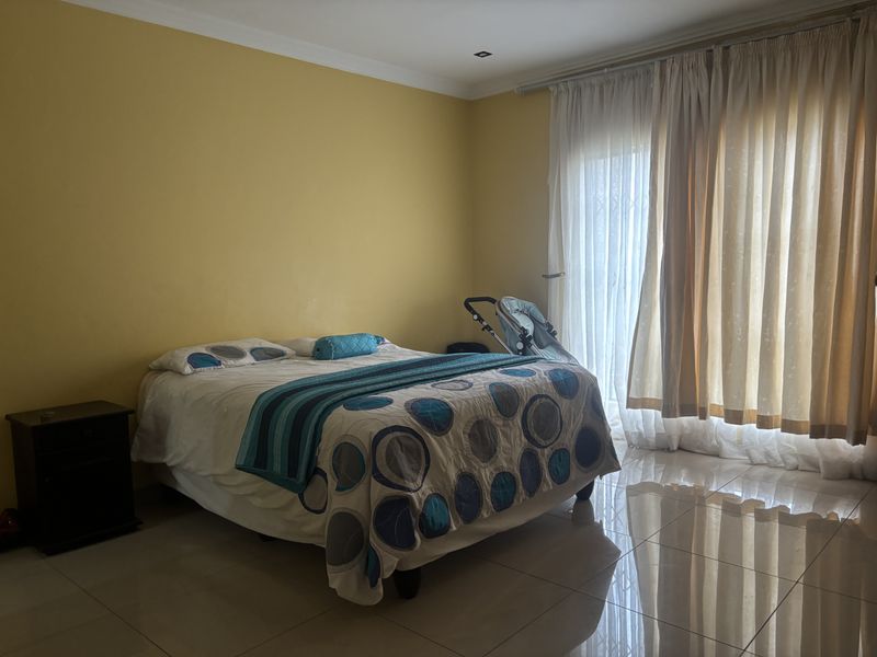 A spacious bedroom featuring tiled flooring, recessed lighting, and a sliding glass door with security gate providing access to the exterior.