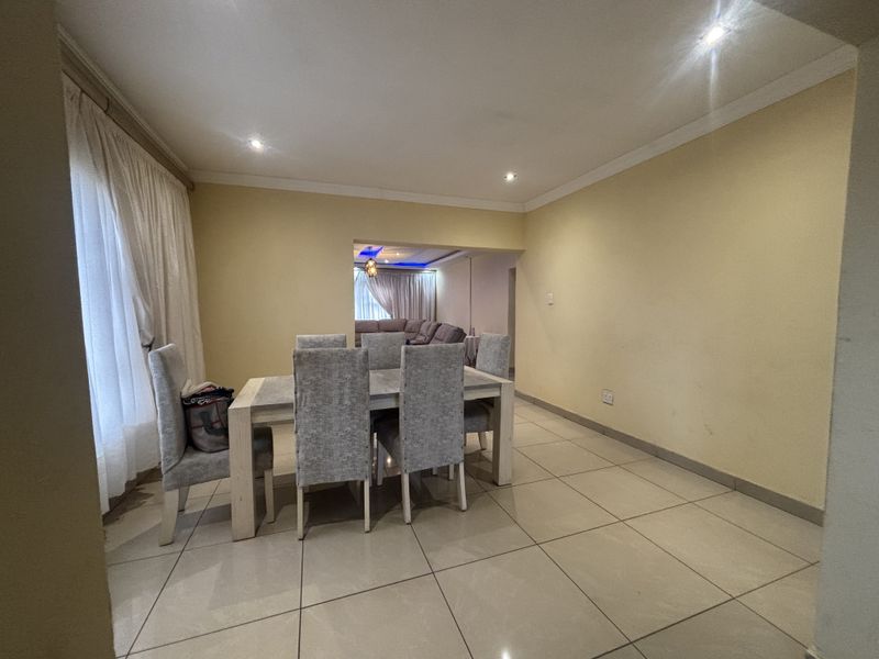 A spacious dining area featuring neutral tiled flooring, recessed downlighting, and coved cornicing, with an open-plan flow into the adjacent living space.