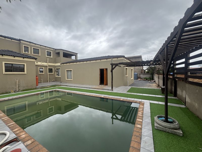 Rear exterior view featuring a swimming pool with tiled surround, artificial turf, and a timber pergola structure against the house facade.