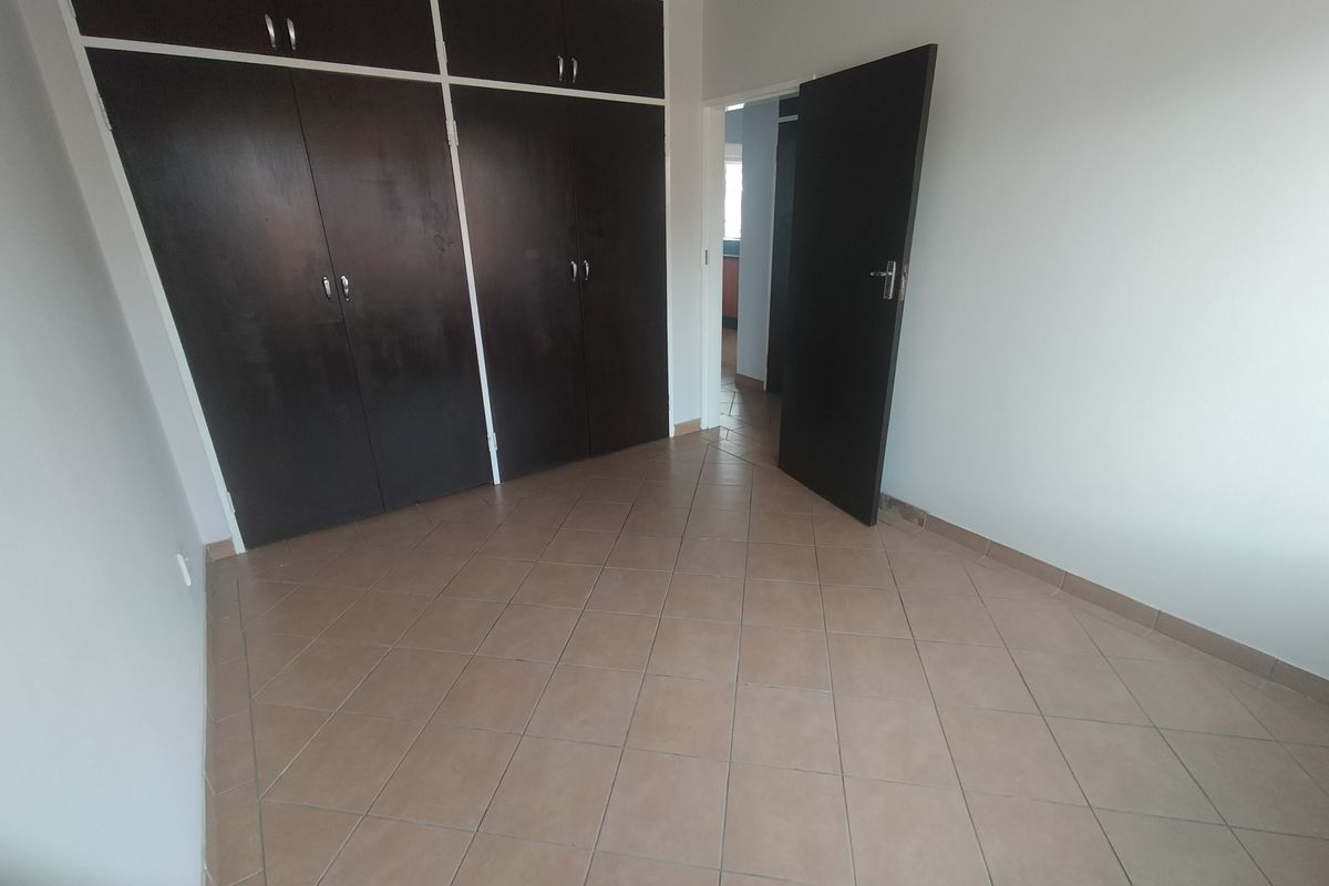 An empty bedroom featuring dark built-in cupboards and neutral tiled flooring, offering a blank canvas for personalization.