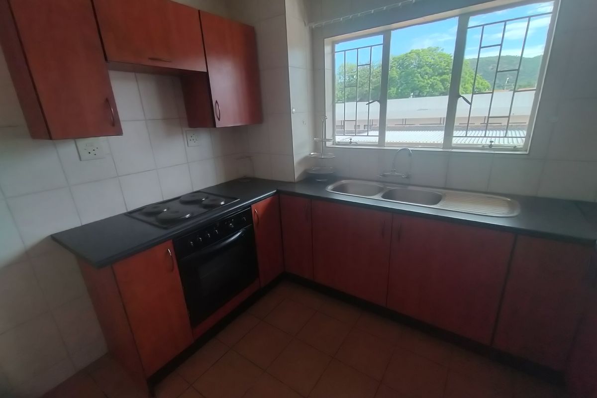 A functional kitchen featuring built-in wooden cabinetry, dark laminate countertops, a double sink, and an integrated electric oven and hob.