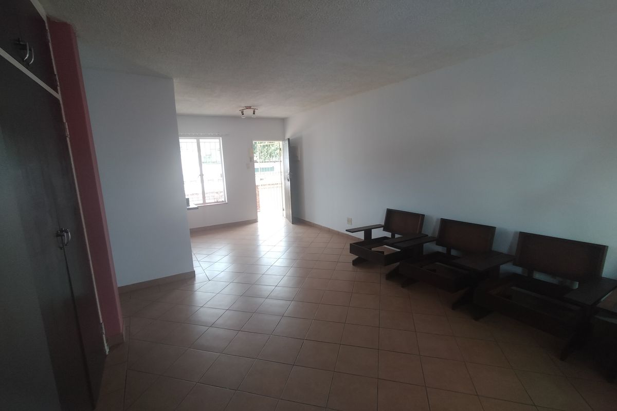 A spacious living area featuring neutral tiled flooring and a built-in cupboard, offering a blank canvas for interior design updates.