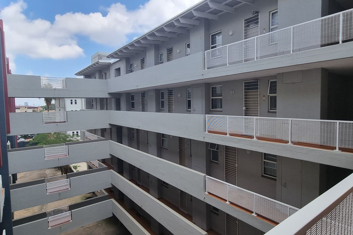 Exterior view of a multi-story apartment complex featuring concrete walkways, metal balustrades, and access to individual units.