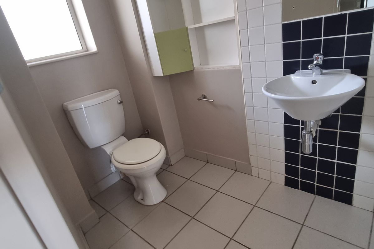 A functional bathroom featuring a wall-mounted basin with a tiled splashback, a standard toilet, and built-in shelving.