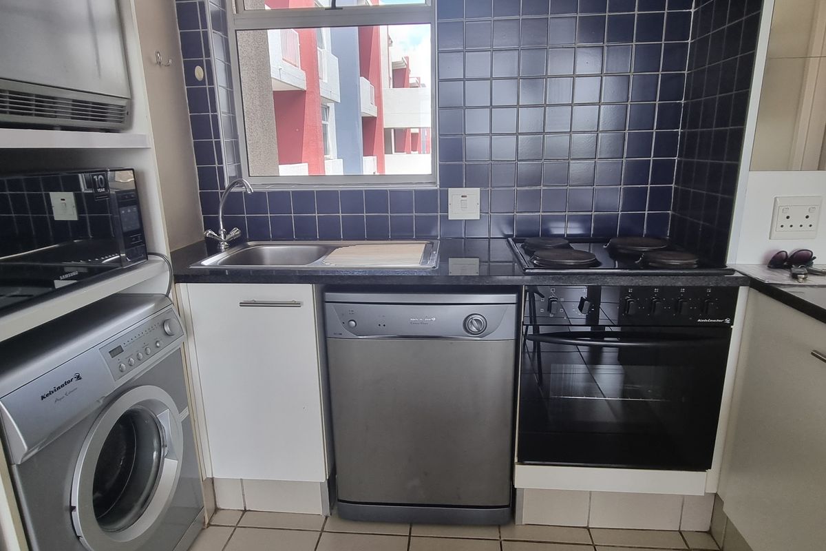 Compact kitchen featuring dark tiled splashbacks, granite countertops, built-in oven, electric hob, and integrated laundry plumbing.