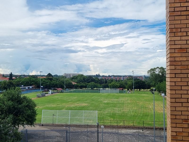 An elevated view overlooking a sports field and surrounding neighbourhood, framed by the brick exterior of the building.